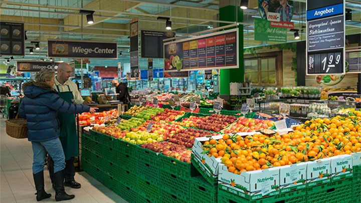 Clienţi uitându-se la fructele expuse la Real, sub lumina sistemelor de iluminat pentru supermarketuri de la Philips