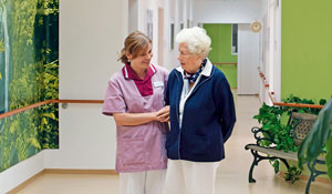 Asistentă îngrijind o doamnă în vârstă pe un culoar iluminat