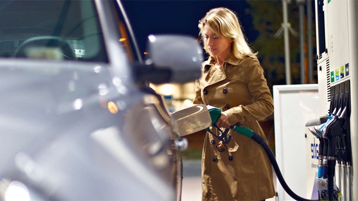 O femeie își alimentează automobilul la o pompă intens luminată de o instalație Philips.