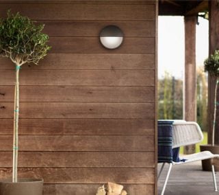 Aplica de perete modernă cu LED pentru exterior luminează exteriorul rustic din lemn, fiind o soluție de iluminat eficientă din punct de vedere energetic și rezistentă la intemperii pentru fațadele caselor și verande contemporane.